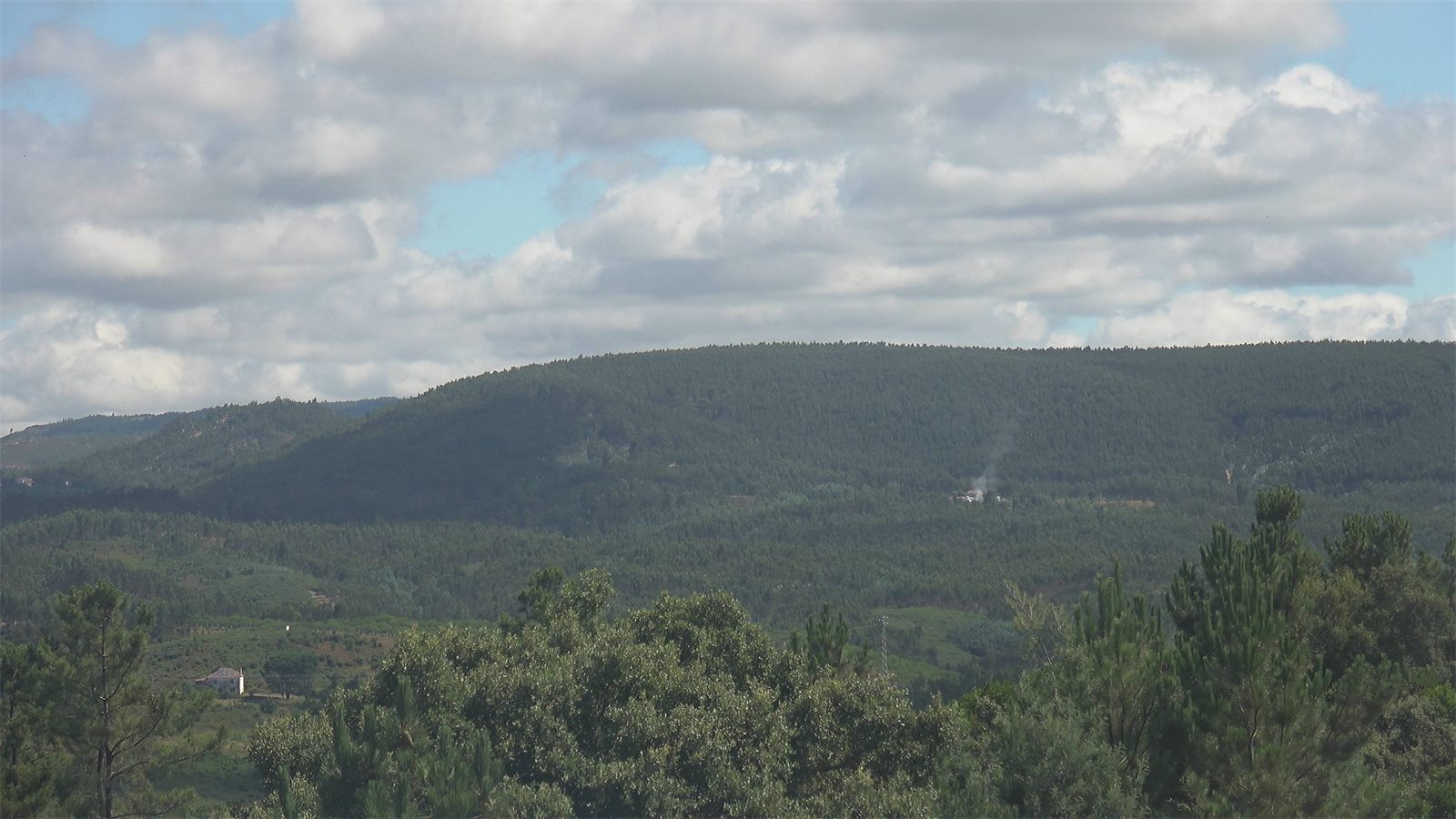 Camera frame: first smoke beside a farmhouse in a forested valley, marked by the AI