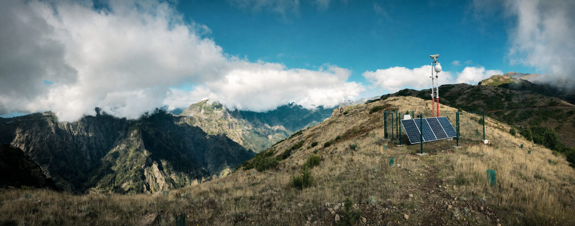 A SafeForest camera tower with solar panels on a mountain ridge above deep valleys